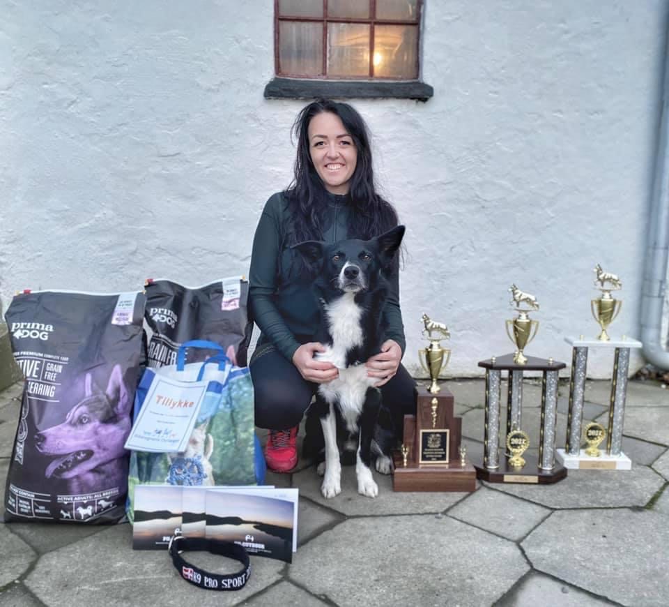 Happy woman with her border collie dog, celebrating dog training success with trophies and dog food.